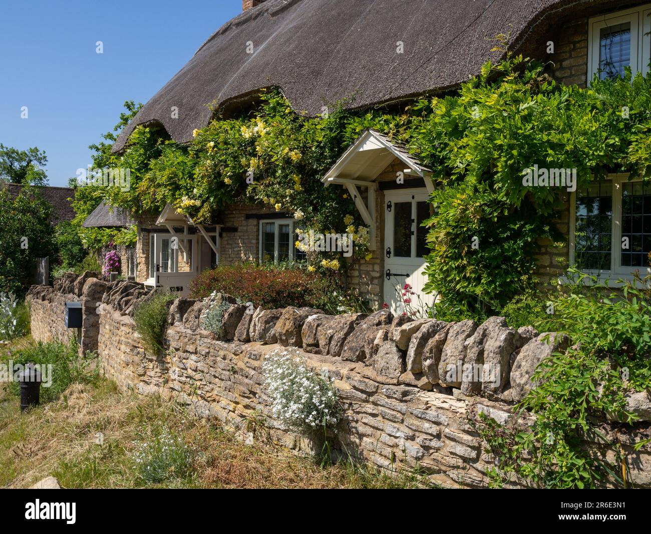 Attraktives strohgedecktes Cottage im Sommer mit Rosen um die Tür, im Dorf Ravenstone, Buckinghamshire, Großbritannien Stockfoto