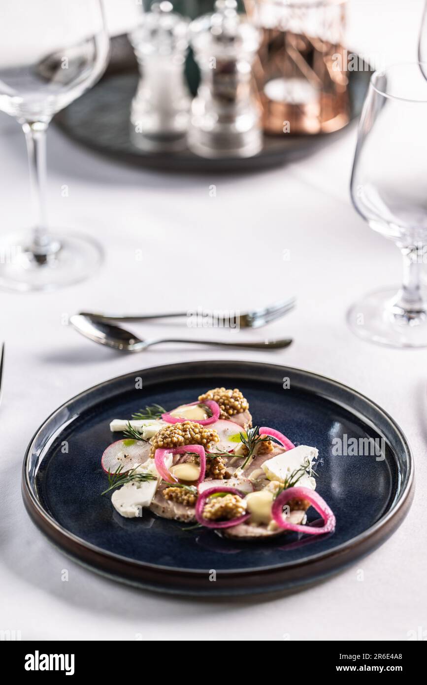 Vorspeise im Restaurant mit Enten- oder Gänseleberpastete mit Gemüse auf einem dunklen Teller und einem weißen Tisch. Stockfoto