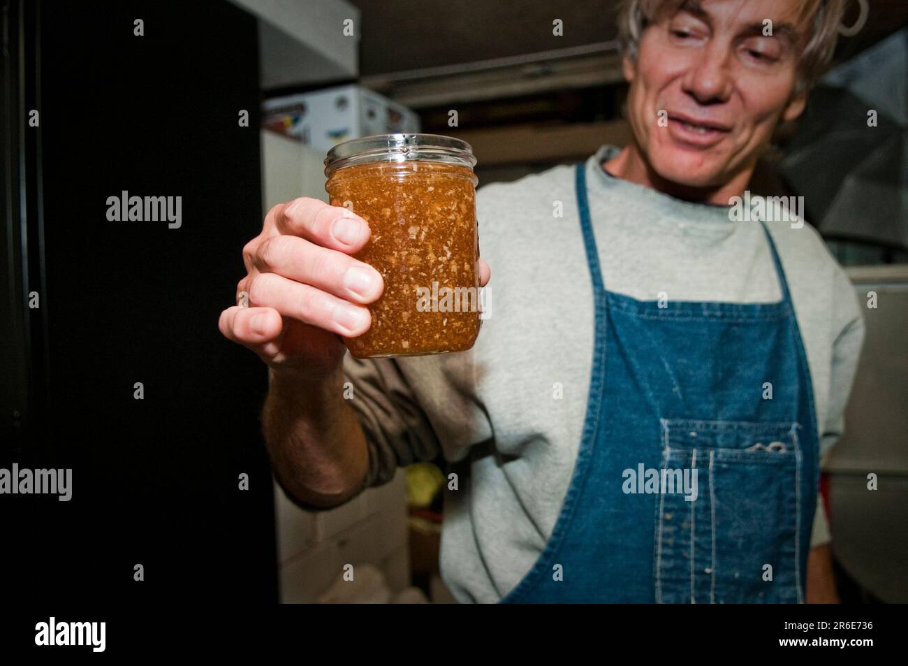 Ein Mead-Maker hält ein Glas rohen, ungefilterten Honig, um die goldene Farbe zu bewundern. Stockfoto