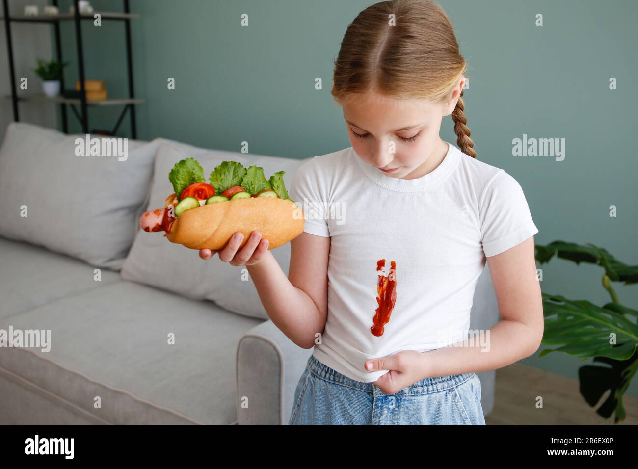 Das Kind hat seine Kleidung mit Ketchup befleckt. Ein Mädchen isst einen Hot Dog. Stockfoto