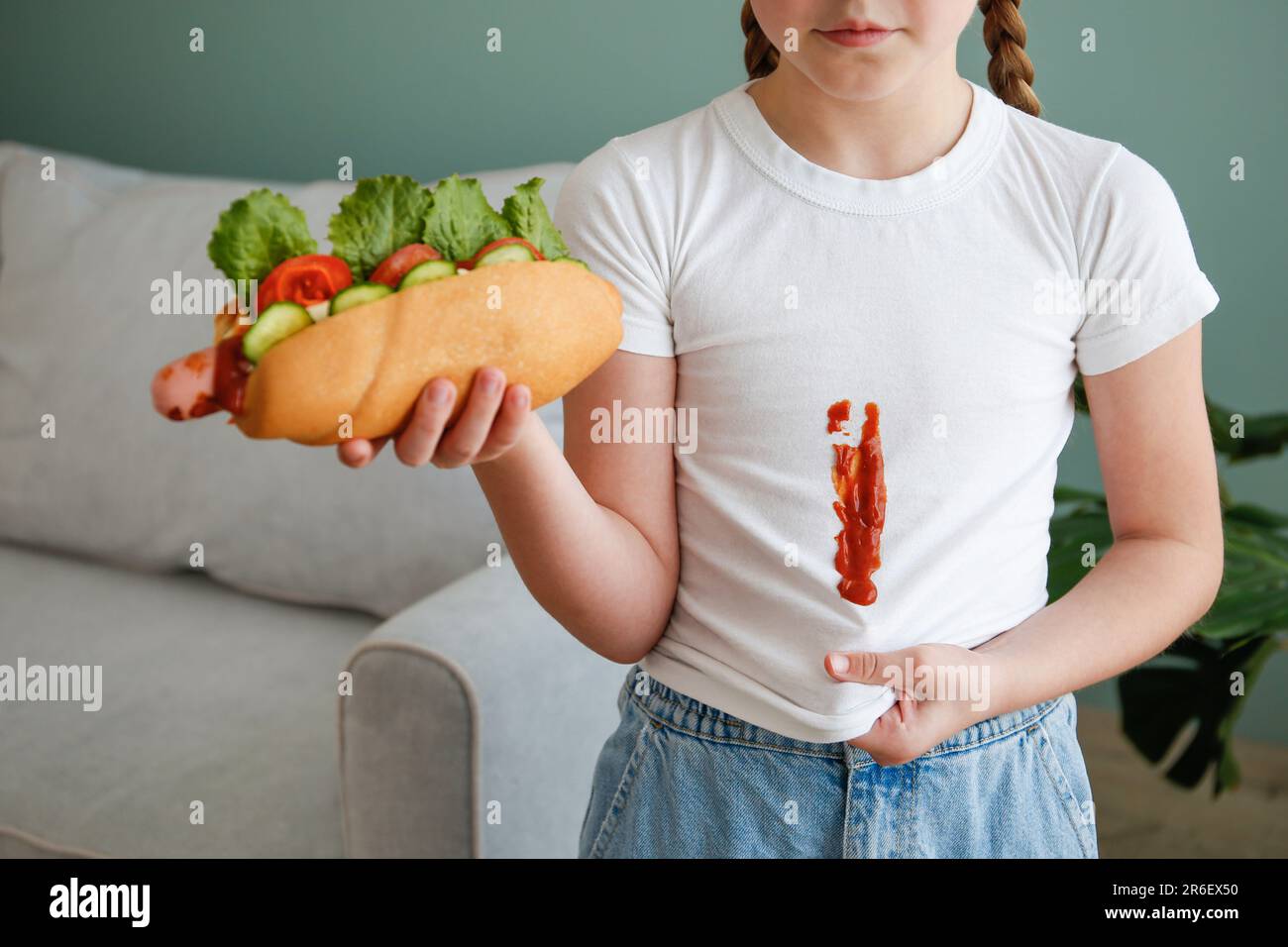 Das Kind hat seine Kleidung mit Ketchup befleckt. Ein Mädchen isst einen Hot Dog. Stockfoto