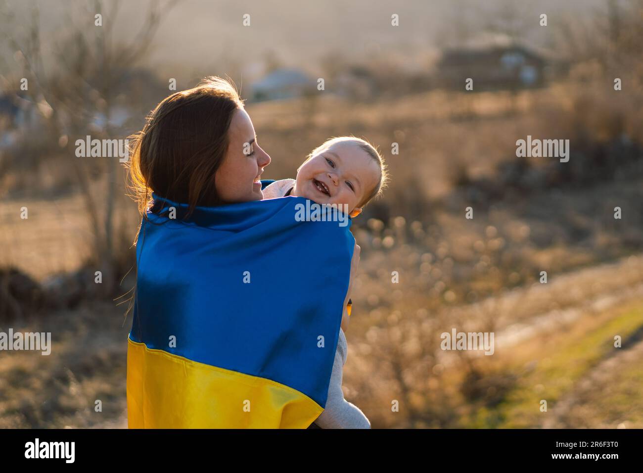 Eine Frau umarmt ihren kleinen Sohn, eingewickelt in die gelb-blaue Flagge der Ukraine im Freien. Stockfoto