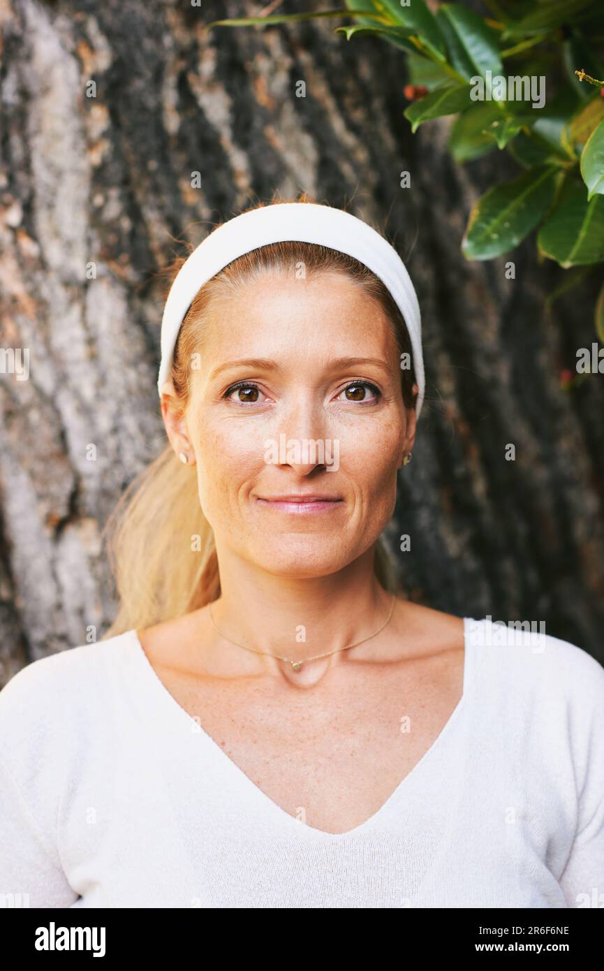 Außenporträt einer erwachsenen Frau in weißer Kleidung, die sich neben dem Baum posiert Stockfoto