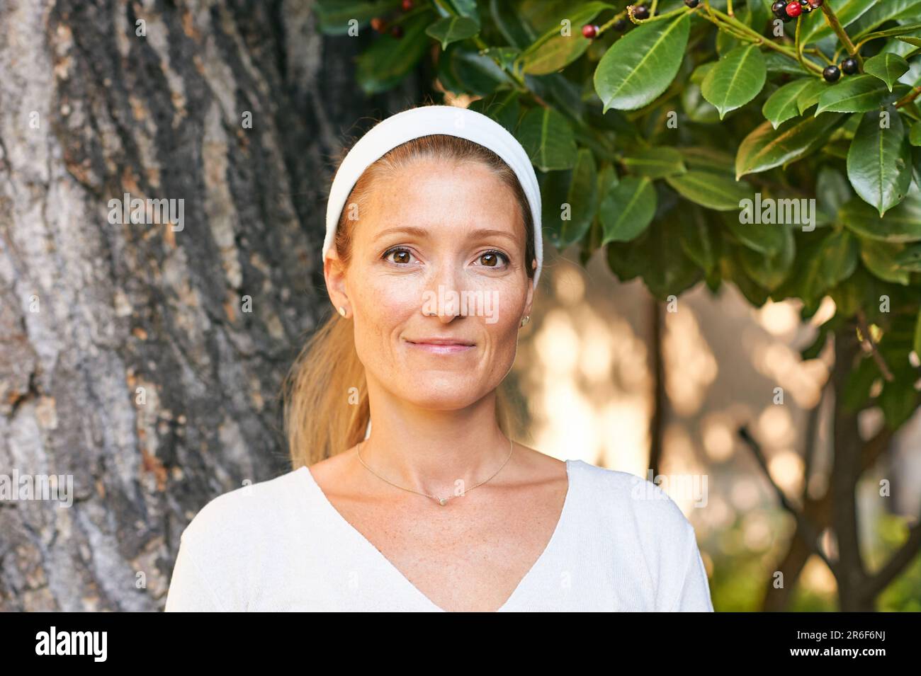 Außenporträt einer erwachsenen Frau in weißer Kleidung, die sich neben dem Baum posiert Stockfoto