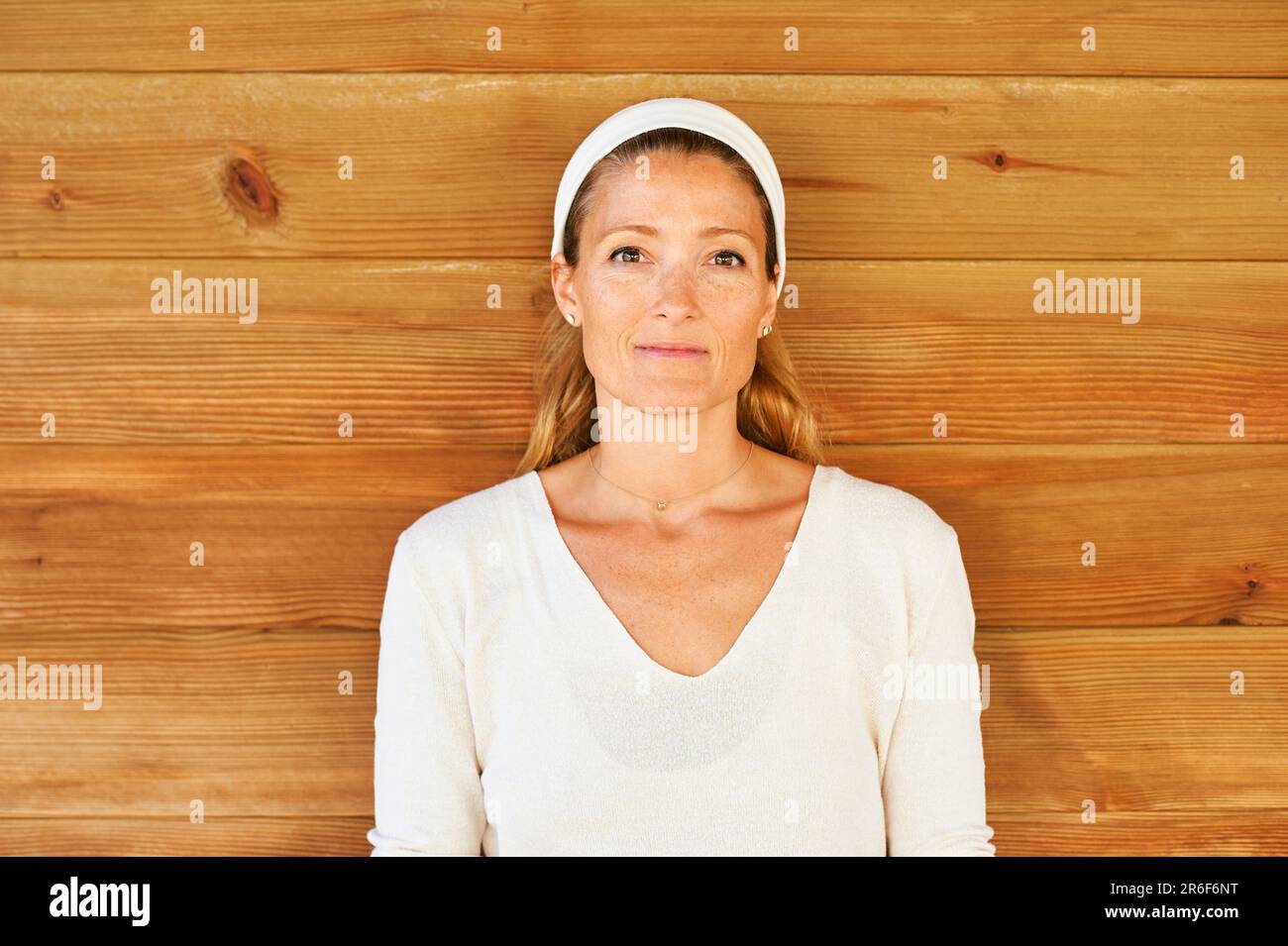 Schöne, reife Frau, die draußen vor einem hölzernen Hintergrund posiert, weiße Kleidung trägt, den Kopf mit einem Band bedeckt Stockfoto