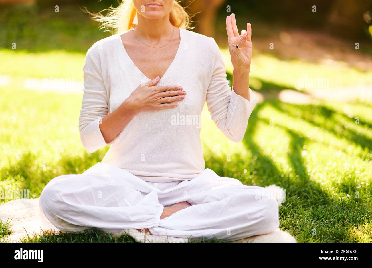 Schöne, reife Frau meditiert im grünen, sonnigen Garten, gesunde Lebensweise Stockfoto