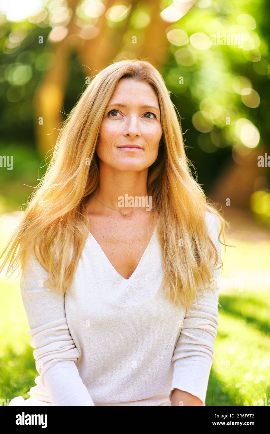 Schöne, reife Frau, die draußen in einem sonnigen Park oder Garten posiert Stockfoto