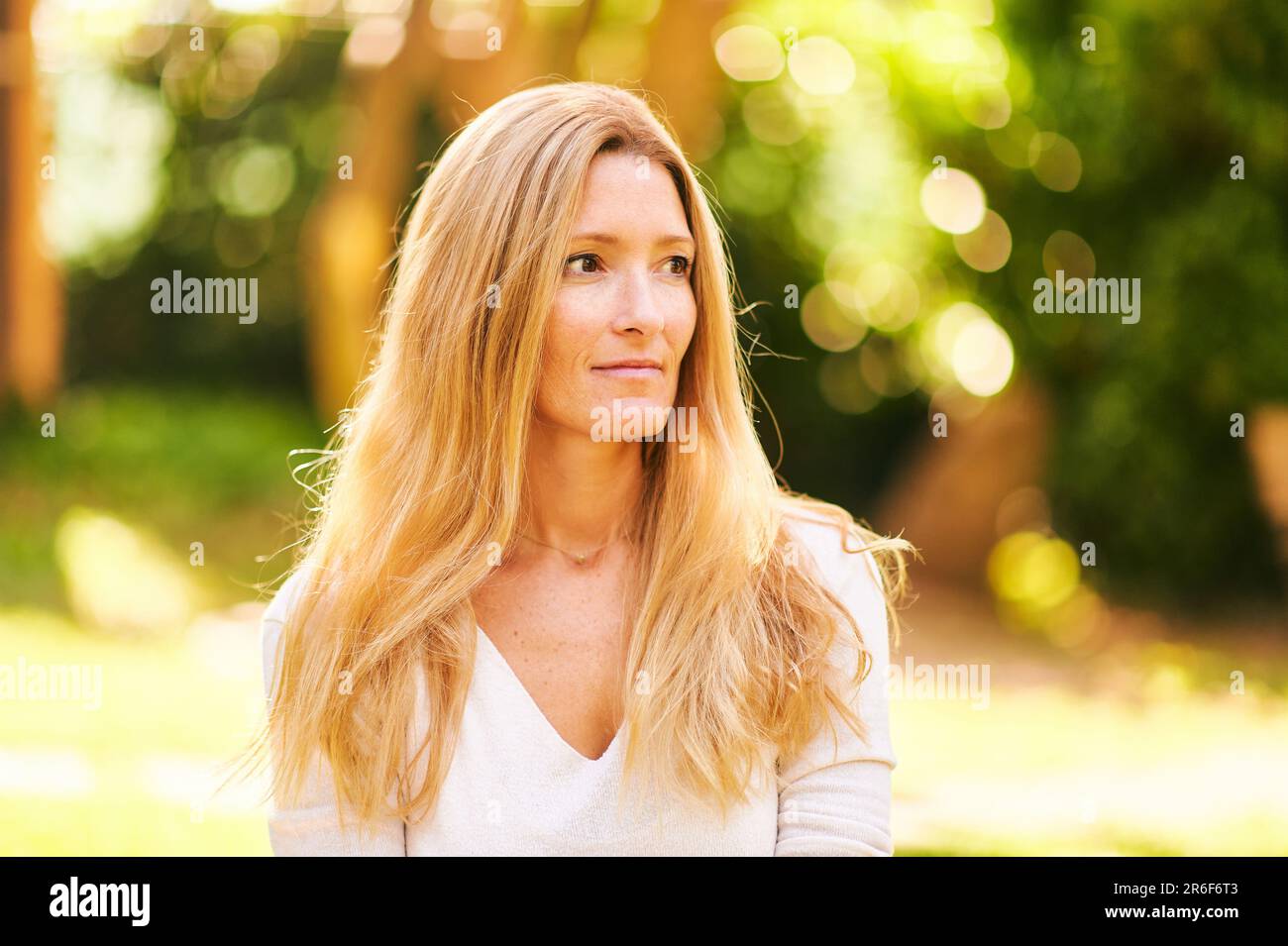 Schöne, reife Frau, die draußen in einem sonnigen Park oder Garten posiert Stockfoto