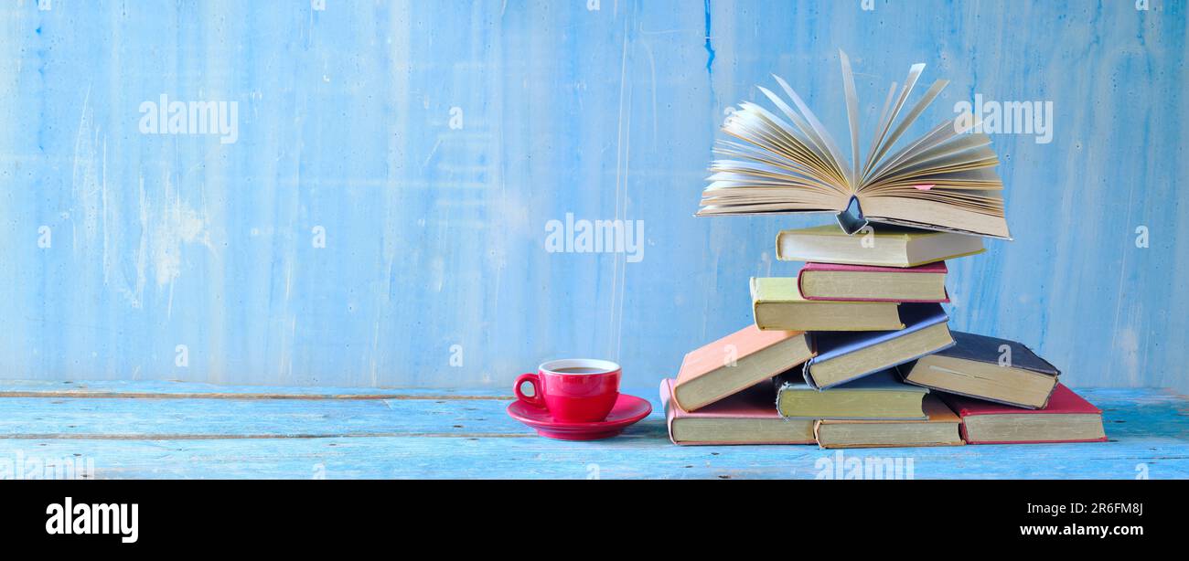 Offenes Buch, Bücher auf Papier und eine Tasse Kaffee auf blauem Hintergrund. Literatur, Bildung, Lesen und Entspannungskonzept. Panorama mit großem Kopierbereich Stockfoto
