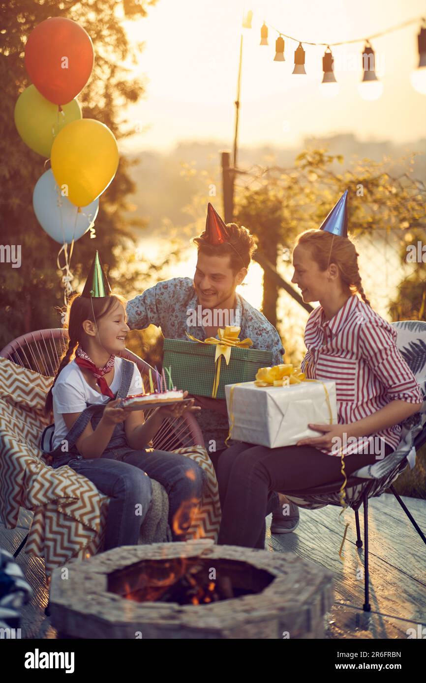 Geburtstagsfeier. Mom und Dad schenken Geburtstagskinder, sitzen draußen am Kamin in einem gemütlichen Cottage. Feier, Lifestyle Conc Stockfoto