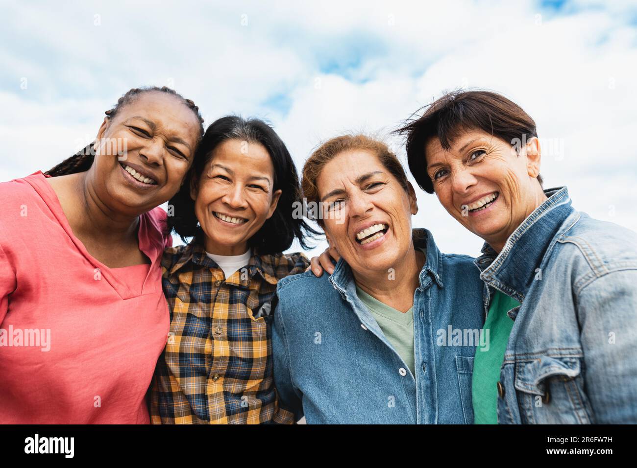 Glückliche, multiethnische Seniorinnen, die Spaß haben, auf dem Dach des Hauses in die Kamera zu lächeln Stockfoto