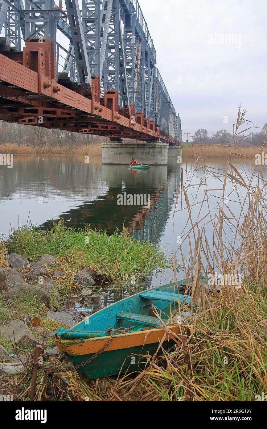 Ein Fischerboot, das im Schilf unter einer Eisenbahnbrücke auf einem Fluss namens Southern Bug festgemacht hat. Stockfoto