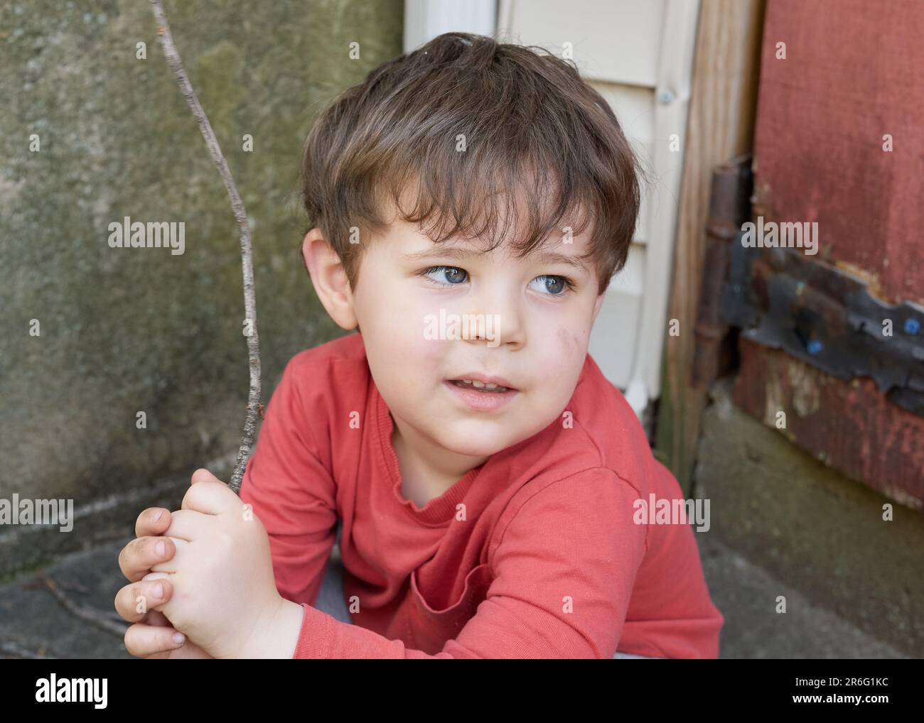 Süßer kleiner Junge, der mit Zweigen im Garten bei der Garage spielt Stockfoto