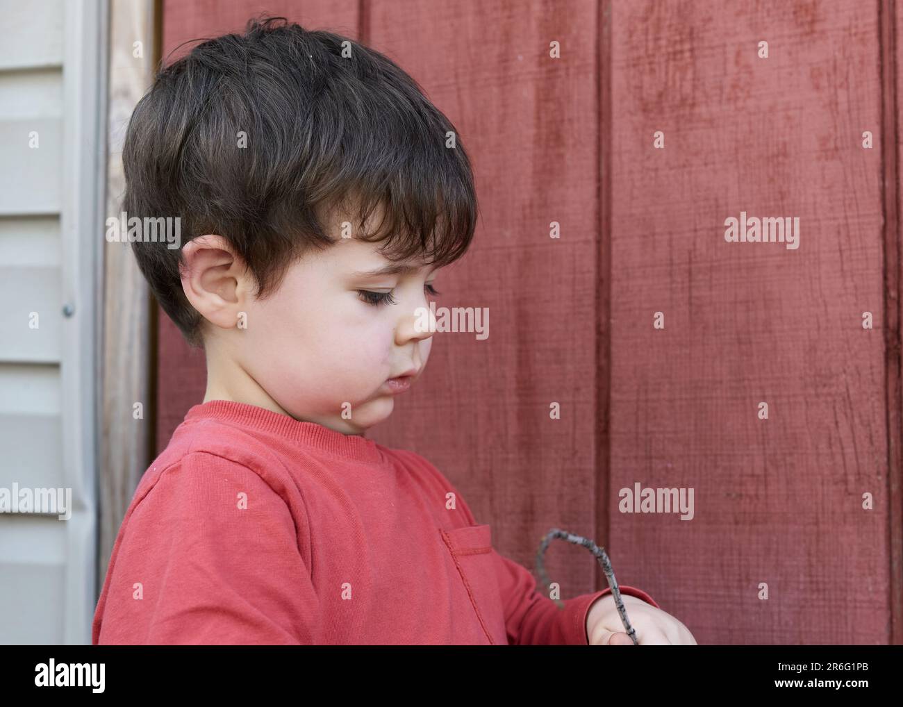 Süßer kleiner Junge, der mit Zweigen im Garten bei der Garage spielt Stockfoto