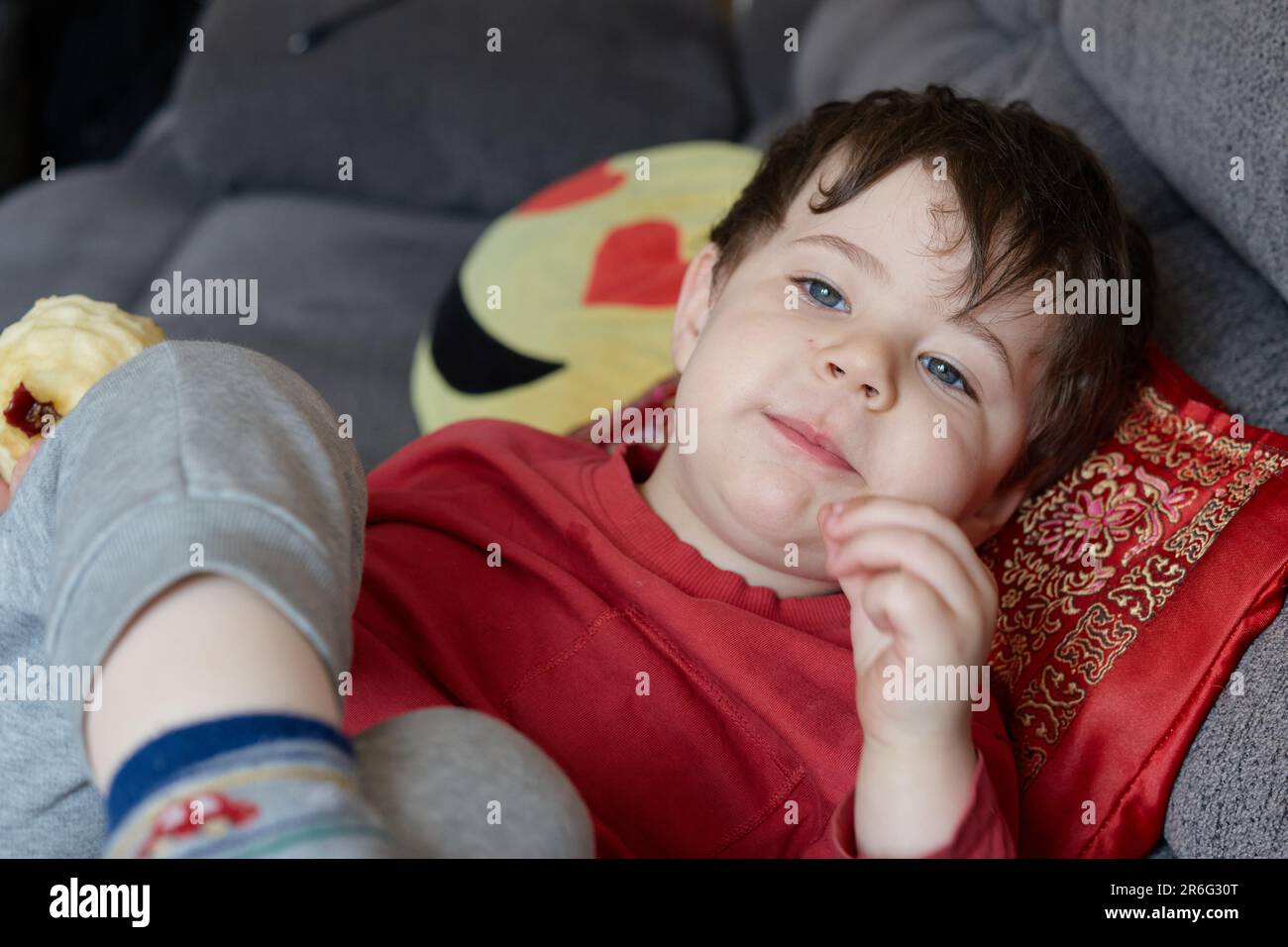 Ausdrucksstarker Junge, der einen Apfel isst und sich zu Hause auf der Couch ausruht Stockfoto