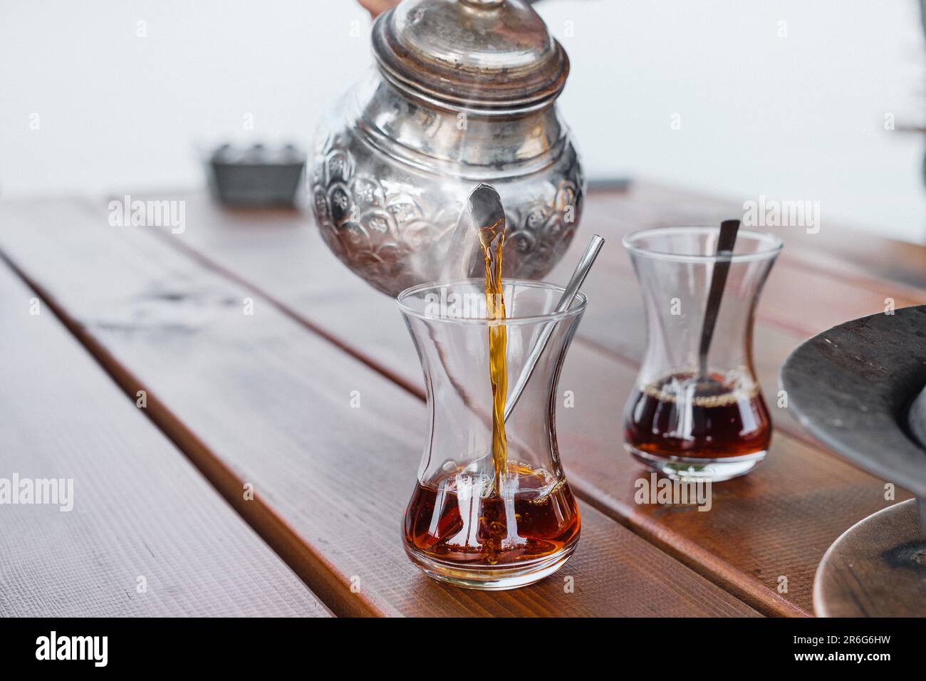 Tee wird in ein Glas aus einer traditionellen türkischen Teekanne gegossen, selektiver Fokus, Dampf aus dem heißen Getränk aufsteigt. Frühstück in einem Café, Reisen und Ausruhen Stockfoto