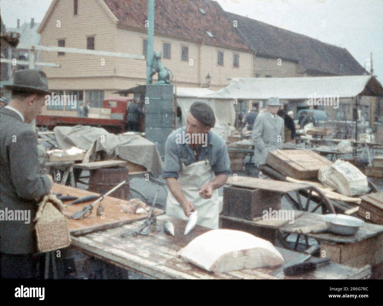 1950er, Bergen, Norwegen - ein Fischhändler filet für einen Touristen im Hafen von Bergen, Löwenstatue im Hintergrund Stockfoto 1950er, Bergen, Norwegen - ein Fischhändler filet für einen Touristen im Hafen von Bergen, Löwenstatue im Hintergrund Stockfoto