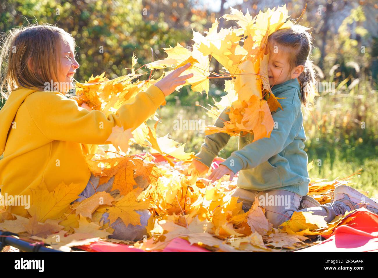 Mädchen, die auf Trampolin mit Herbstblättern springen. Leuchtend gelbes Ahornblatt. Kinder laufen, haben Spaß im Herbstgarten. Draußen Stockfoto