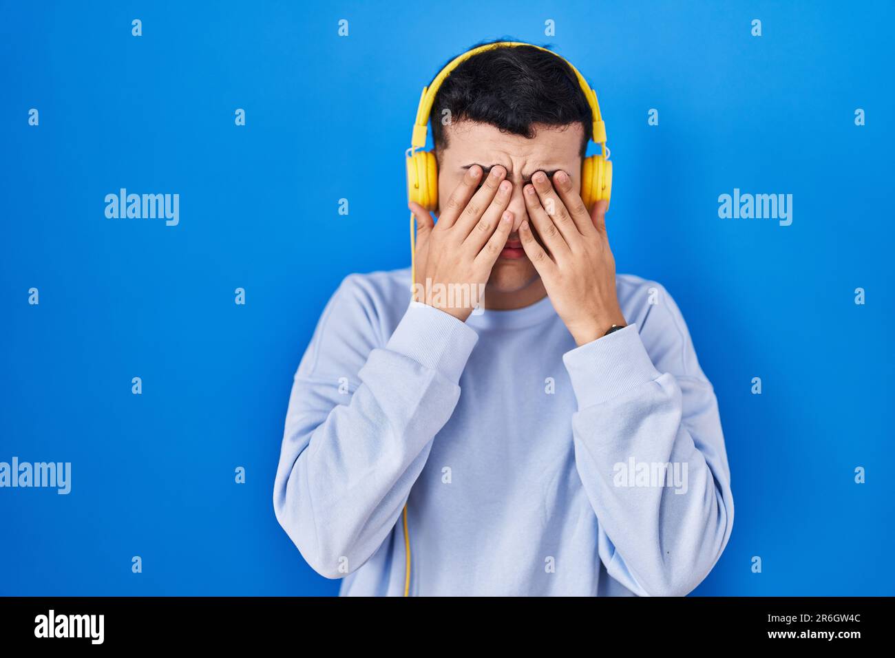 Nicht binäre Person, die Musik über Kopfhörer hört und die Augen reibt, um Müdigkeit und ...