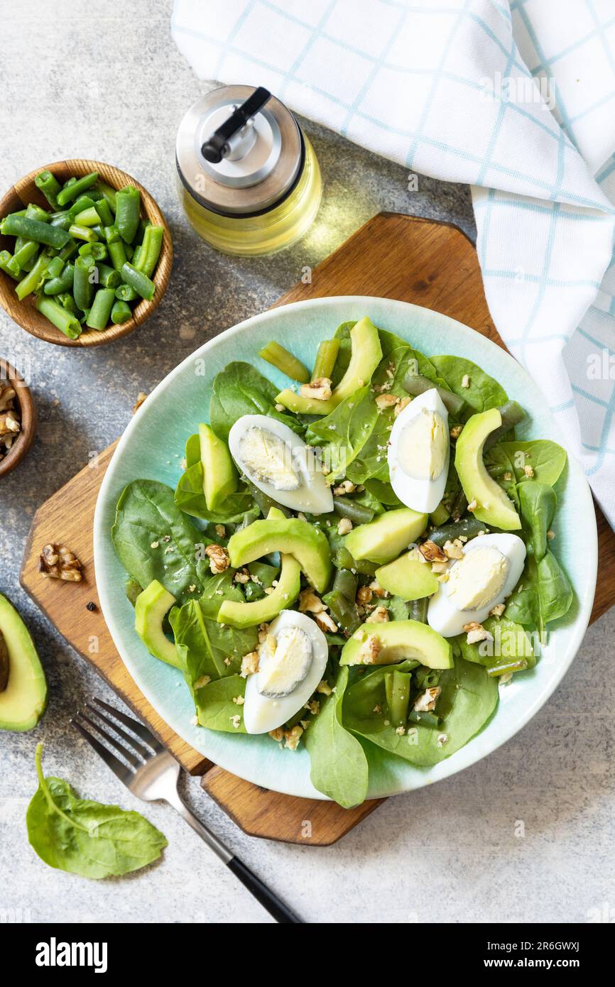 Gesundes Essen, Sommer gesundes Essen. Bio-Avocado und Spinatsalat mit Eiern, grünen Bohnen, Nüssen auf einem Steintisch. Blick von oben. Stockfoto