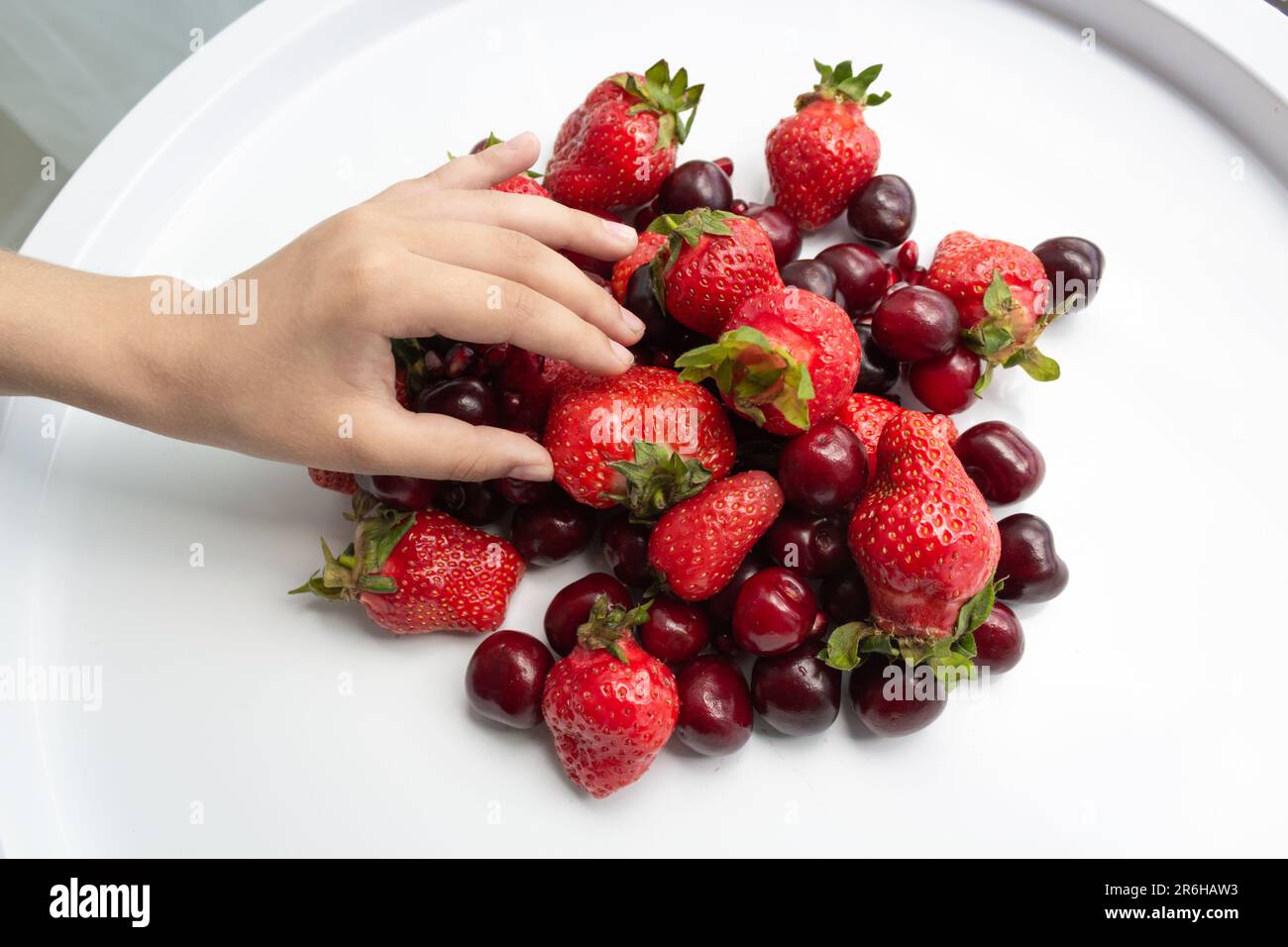 Weißer Tisch mit frischen Erdbeeren und Kirschen, Frauenhand Stockfoto