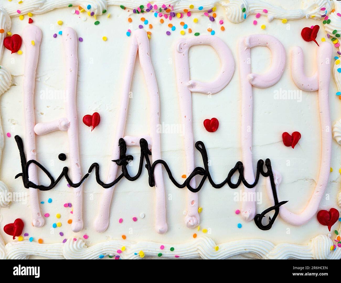„Happy Birthday“-Text auf weißem Kuchen mit roten Herzen und bunten Streuseln Stockfoto