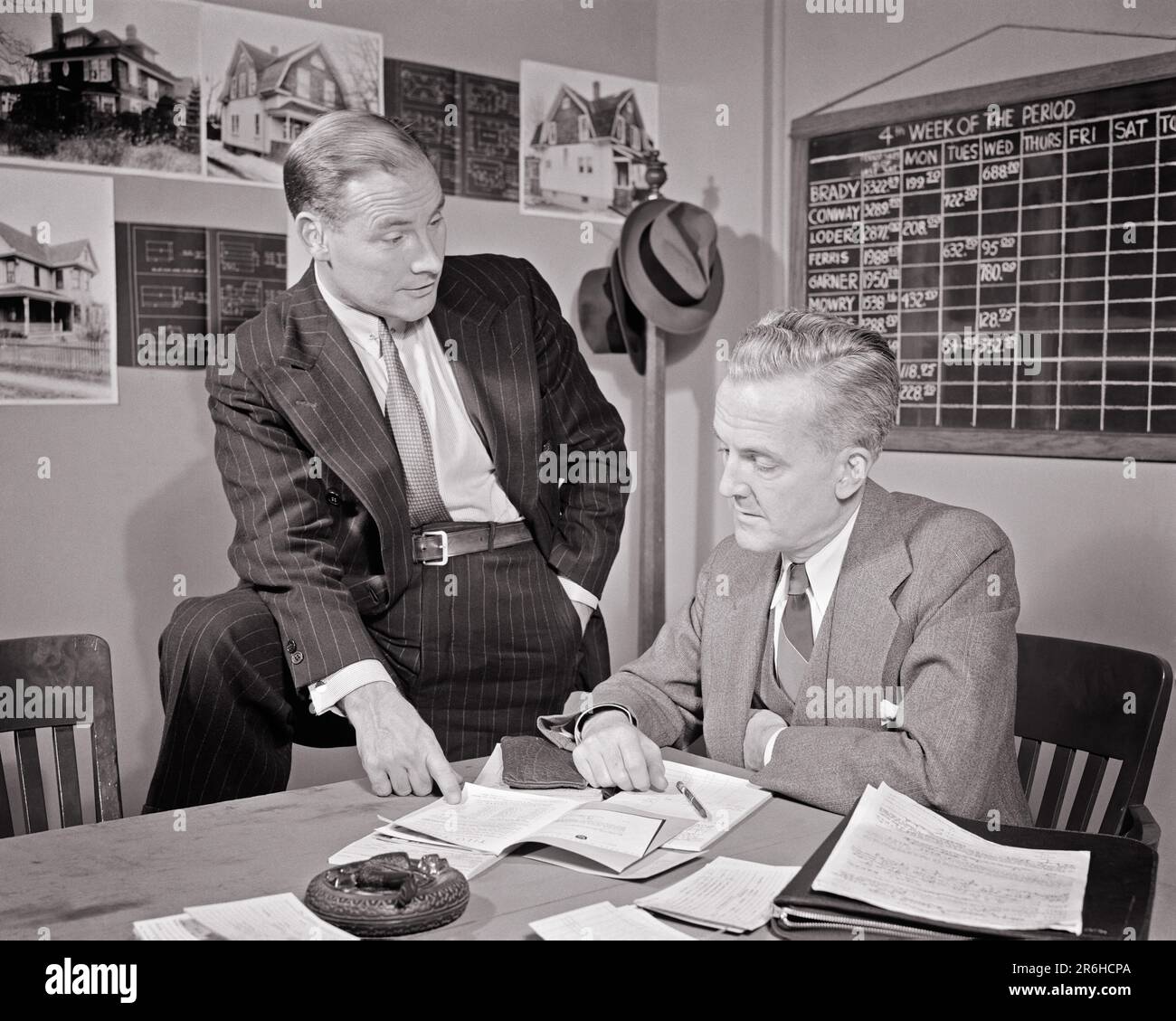 1930S 1940S ZWEI IMMOBILIENMAKLER IM BÜRO, DIE PAPIERFOTOS VON HÄUSERN AN WÄNDEN UND KREIDETAFELN DURCHGEHEN ZEITPLAN - O1676 HAR001 HARS TEAMWORK INFORMATIONEN FOTOS LIFESTYLE ARCHITEKTUR HÄUSER JOBS KOPIEREN PLATZ HALBLANG MÄNNER GEBÄUDE ECHTE WESTE MITTLEREN ALTERS B&W MÄNNER MITTLEREN ALTERS ZIELE QUALIFIKATIONSANZUG UND KRAWATTE BESCHÄFTIGUNG SELLING SKILLS IMMOBILIENSTRATEGIE UND ARBEITSMÖGLICHKEITEN BESCHÄFTIGUNG JOBS PLANEN REAL DREITEILIGE ANZÜGE VON ESTATE REALTOR STILVOLLE AGENTEN GEBÄUDE MITARBEITERZUSAMMENARBEIT MITTELERWACHSENER MANN NADELSTREIFENANZUG IMMOBILIENVERKÄUFER ZUSAMMENGEHÖRIGKEIT SCHWARZ UND WEISS Stockfoto