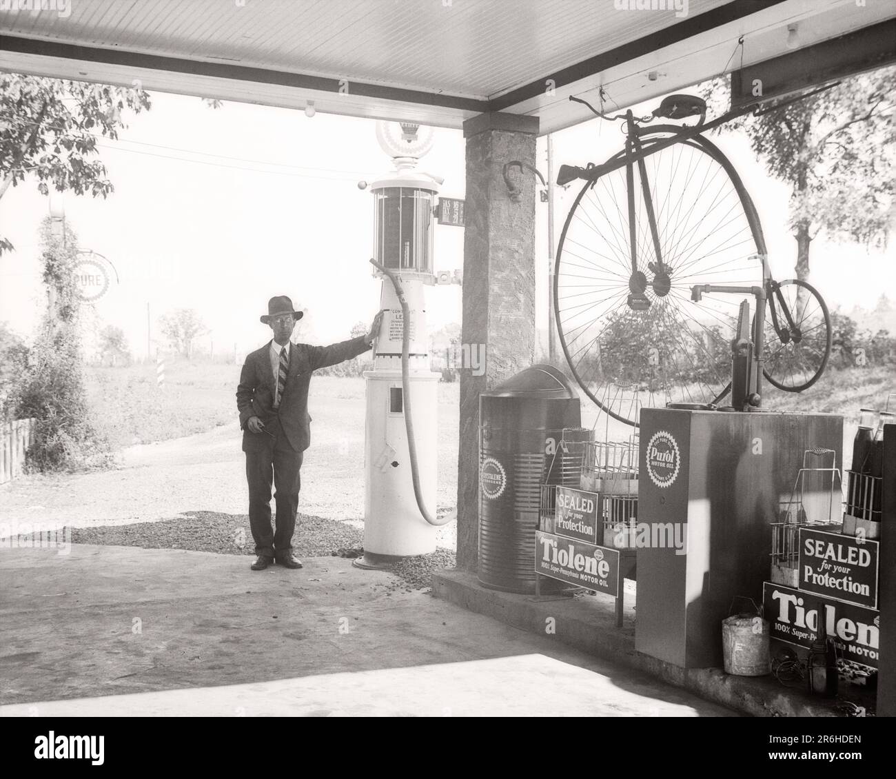 1940S-MANN-BESITZER, DER SICH AN DER TANKSTELLE MIT EINER TANKSTELLE MIT EINEM ANTIKEN PENNY-FARTHING-BIKE UND EINEM MUSKETEN-SCHLANGENHÜGEL IN OHIO BEDIENT USA - Q43998 CPC001 HARS KOPIERRAUM VOLLE LÄNGE PERSONEN UNITED STATES OF AMERICA MÄNNER KRAFTSTOFF VERTRAUEN FAHRRÄDER TRANSPORT B&W MITTLEREN ALTERS BIKES NORDAMERIKA MANN MITTLEREN ALTERS NORDAMERIKANISCHE ALTERS ÄLTERE TANKSTELLEN TANKSTELLEN TANKSTELLEN TANKSTELLEN TANKSTELLEN TANKSTELLEN ANTIQUITÄTEN BERUFE ÄLTERE BENZINBESITZER OHIO, GEWÖHNLICHER PENNY-FARLING, BENZIN, SCHWARZ-WEISS, WEISS, WEISS, WEISSE ETHNISCHE HERKUNFT, ALTMODISCH Stockfoto