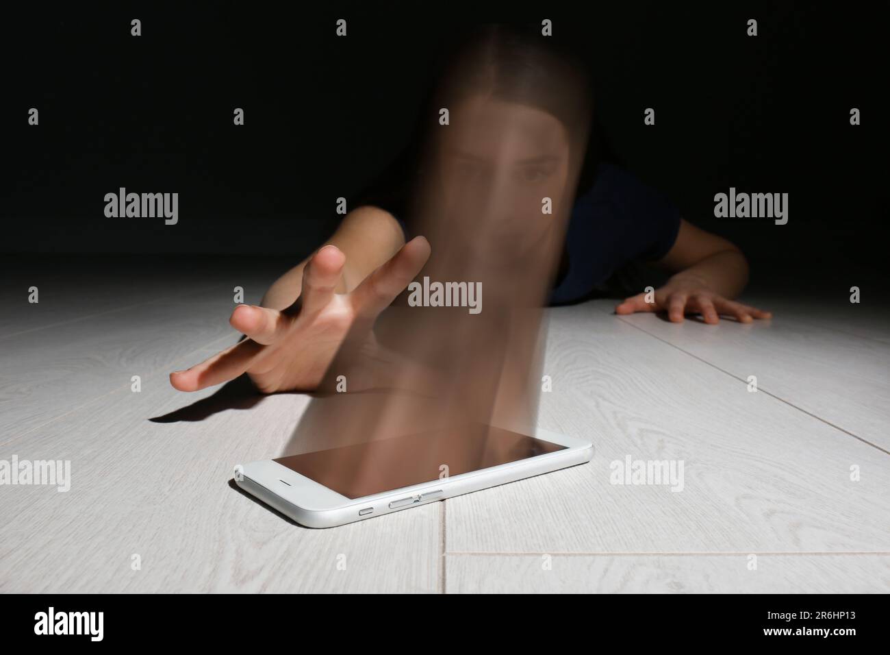 Suchtkonzepte im Internet oder in sozialen Medien. Frau, die auf dem Boden nach einem Smartphone streckt, ihr Gesicht absorbiert von einem Gerät Stockfoto
