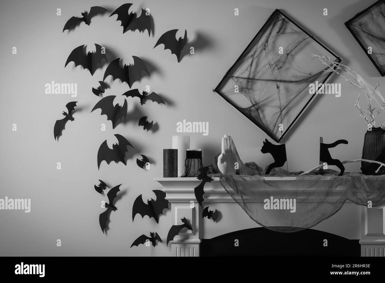 Schwarze Rahmen mit Spinnennetz an den weißen Wänden, Fledermäuse aus Papier und verschiedene Halloween-Dekorationen am Kamin im Innenbereich Stockfoto