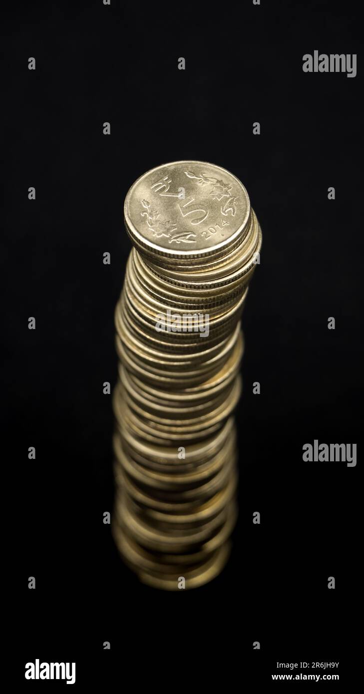 Blick von oben auf glänzende goldene indische 5- oder fünf Rupien-Münzen, die zu einem hohen Turm gestapelt sind, isoliert auf schwarzem Hintergrund Stockfoto