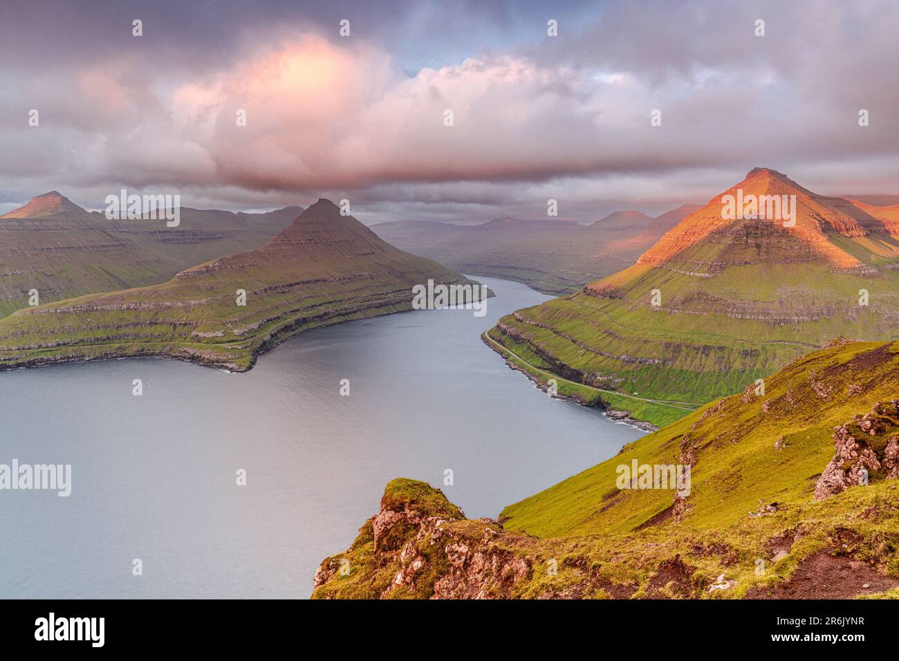 Rosafarbener Sonnenaufgang über Bergen und Klippen entlang des Funningur-Fjords, der Insel Eysturoy, der Färöer, Dänemarks, Europas Stockfoto