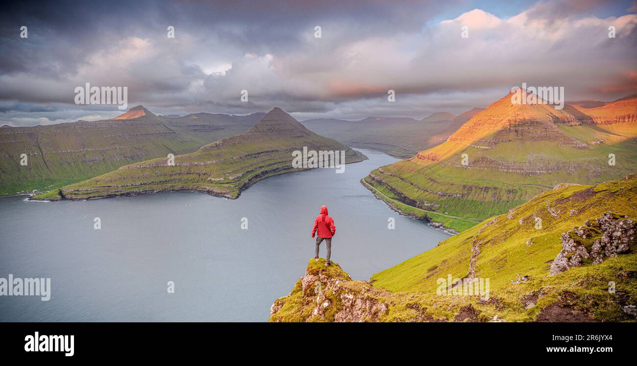 Ein Mann, der den Himmel im Morgengrauen betrachtet und auf Felsen über einem Fjord steht, Eysturoy Island, Färöer Inseln, Dänemark, Europa Stockfoto