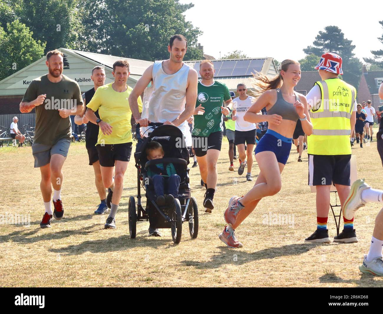 Kesgrave, Suffolk - 10. Juni 2023 : Parkrun an einem heißen, hellen Sommermorgen. Läufer Jung und Alt schnell und langsam, Erwachsene und Kinder. Dad läuft mit einem Baby in einem Buggy. Stockfoto