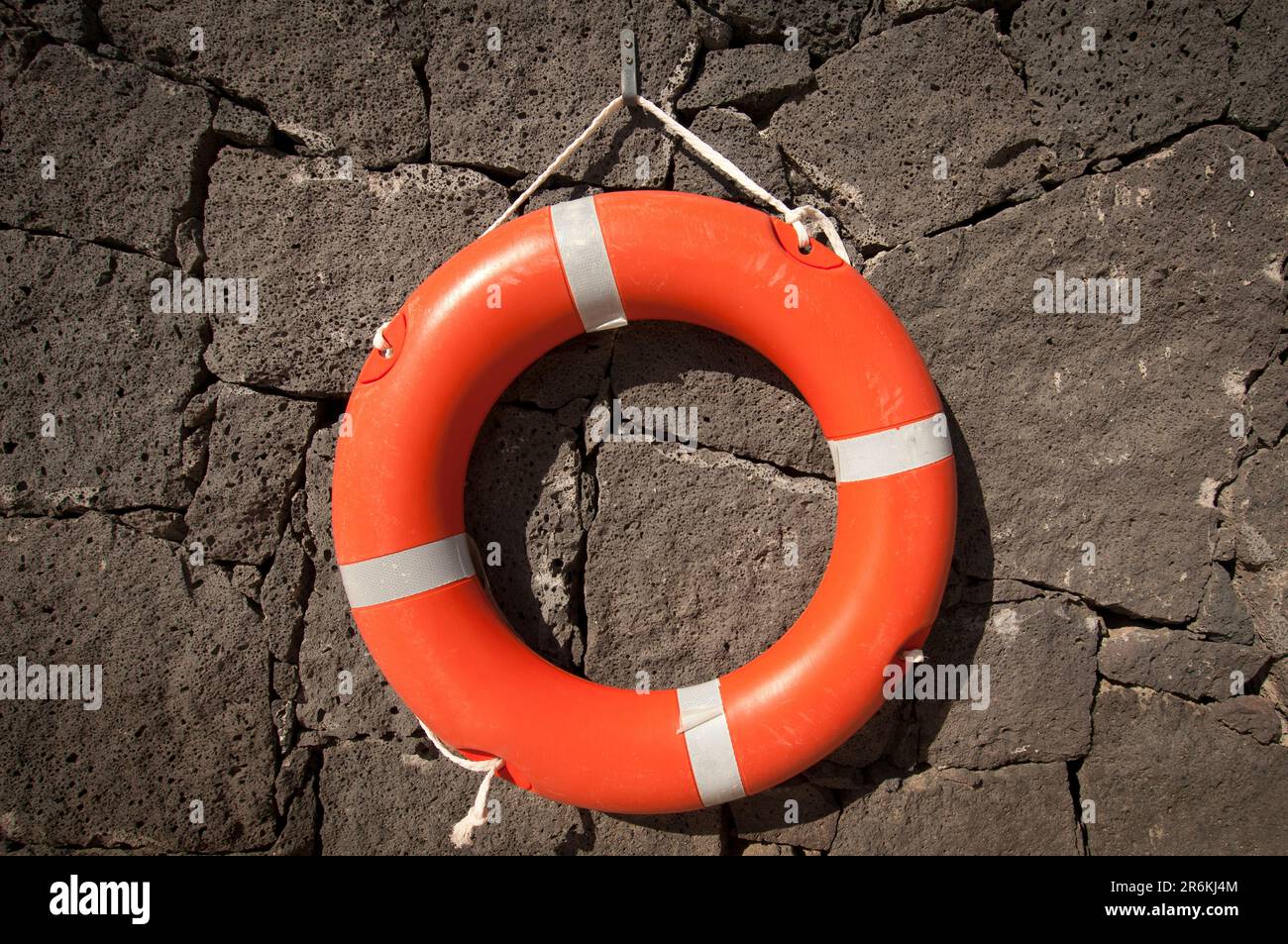 Orangefarbenes Rettungsgürtel, das an einer Steinwand hängt. Stockfoto