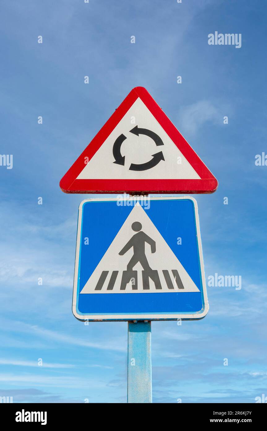 Schilder für Kreisverkehr und Fußgängerübergang vor blauem Hintergrund. Stockfoto