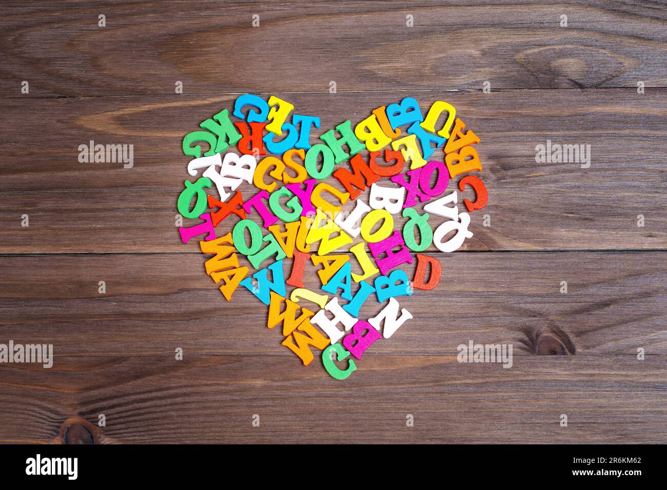 Mehrfarbige hölzerne Buchstaben, die zu einem Herzsymbol auf dunklem Holzhintergrund angeordnet sind. Lebendiges Konzept der Lernmotivation. Stockfoto