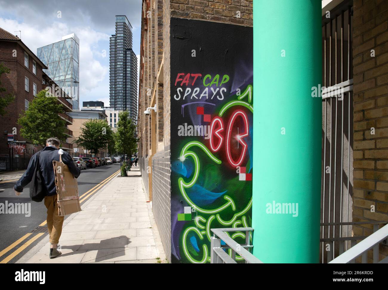 London, Großbritannien - Mai 17 2023: Ein Künstler mit seinem Portfolio geht in Shoreditch die Straße entlang. Die hohen Gebäude des Finanzviertels liegen vor uns. Stockfoto