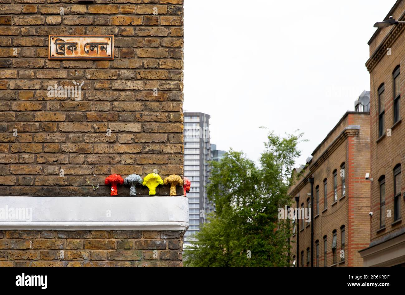 London, Großbritannien - Mai 17 2023: Eine Ecke der Brick Lane mit dem Straßenschild in Bengali und Blumenkohl-Kunstwerken von Adrian Boswell darunter. Stockfoto