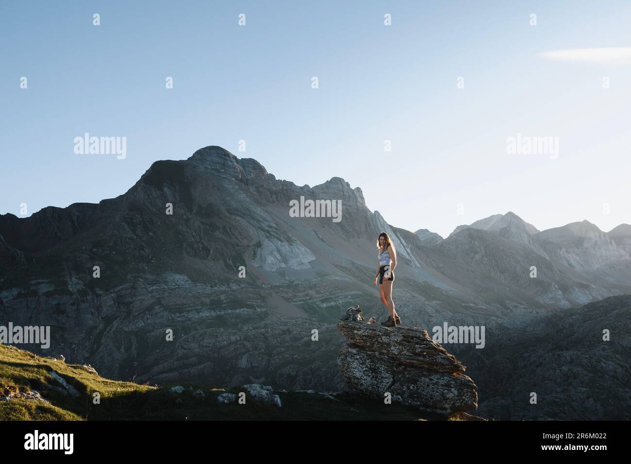 Ein junges Mädchen, das bei Sonnenuntergang auf einen Felsen klettert, mit der Landschaft der pyrenäen im Hintergrund Stockfoto