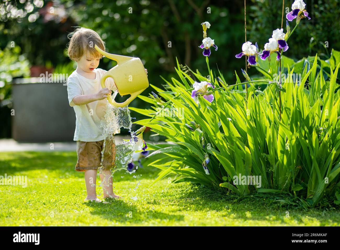Süßes blondes kleines Kleinkind, das im Garten im Gießtopf Pflanzen