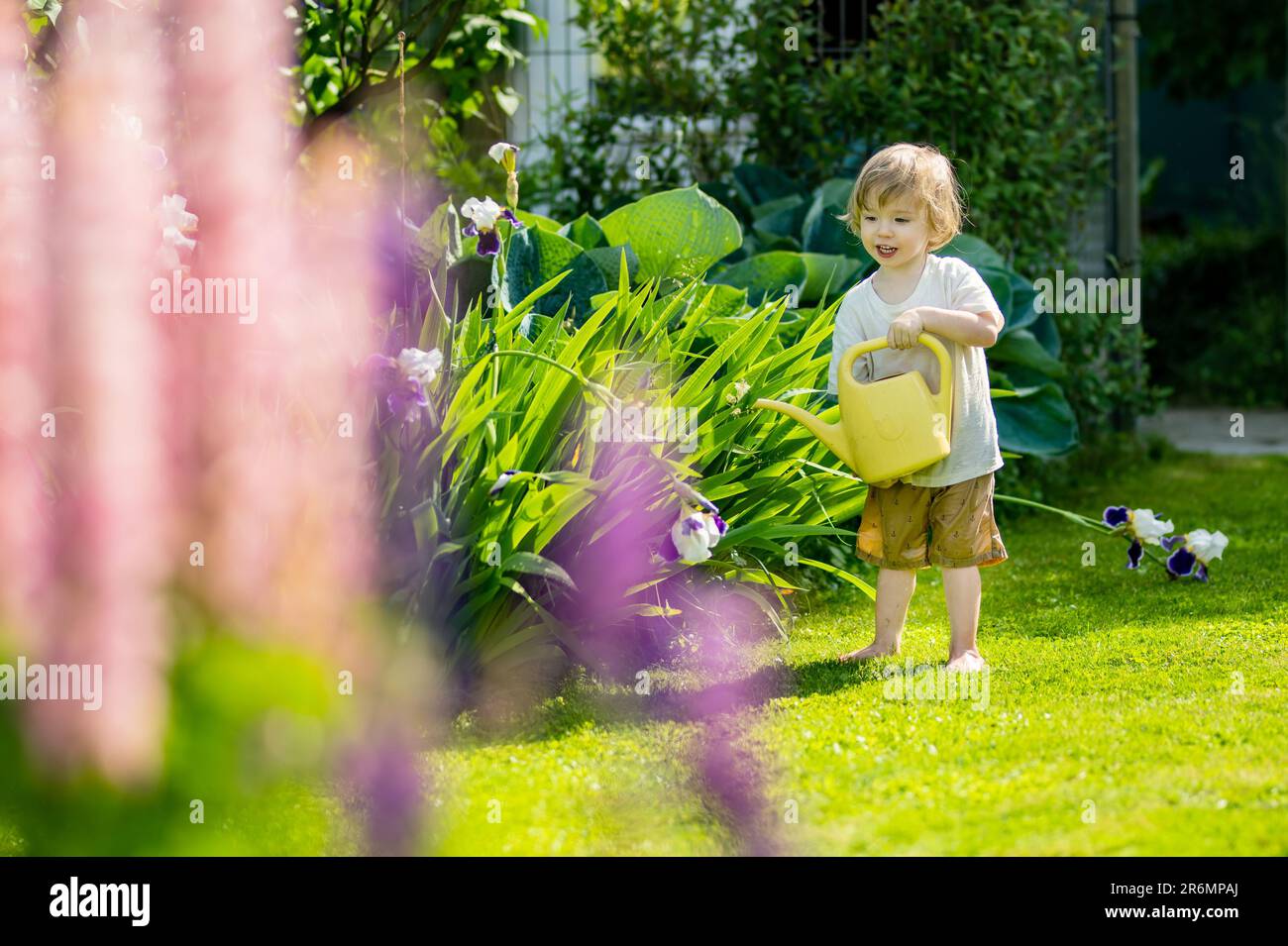 Süßes blondes kleines Kleinkind, das im Garten im Gießtopf Pflanzen