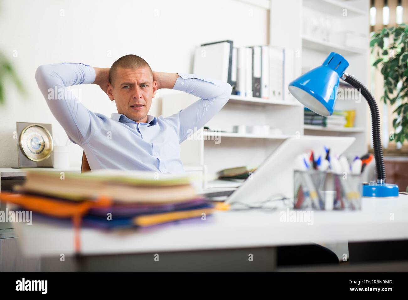 Schockierter Geschäftsmann, der mit vielen Papiermappen am Bürotisch saß Stockfoto