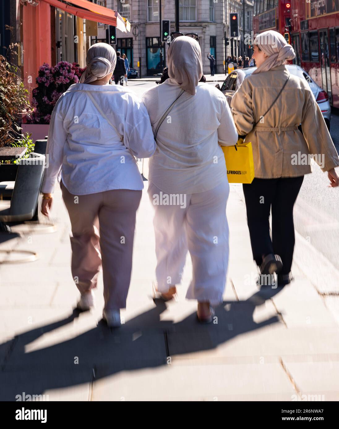 Drei junge Frauen in muslimischen Kleidern, die vor der Kamera entlang Knightsbridge, London, Großbritannien, weglaufen Stockfoto
