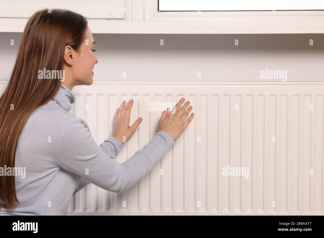 Frau wärmt die Hände am Heizkörper in Innenräumen, Platz für Text Stockfoto