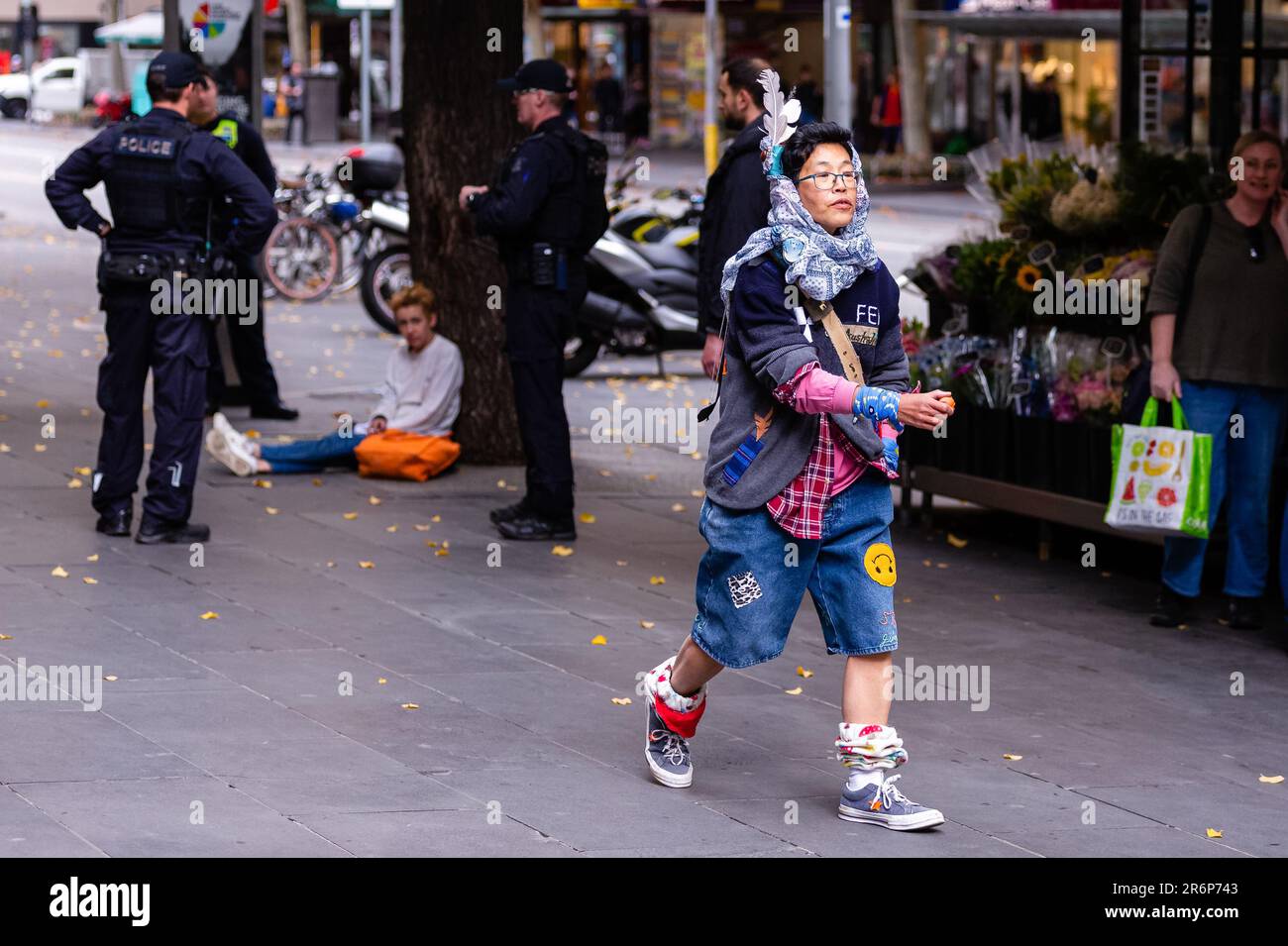 MELBOURNE, AUSTRALIEN - MAI 28: Ein Mann mit einer Feder auf dem Kopf läuft von einer Reihe von Polizisten, die am 28. Mai 2020 in Melbourne, Australien, ein Mitglied der Öffentlichkeit befragten. Als die COVID-19-Krise eskalierte, kündigte Premier Daniel Andrews eine deutliche Erhöhung der Zahl der Polizeibeamten an, die das CBD-Übereinkommen patrouillieren, um die neuen Befugnisse des Notstands durchzusetzen, die am 31. Mai auslaufen. In einem Ausnahmezustand können befugte Beamte auf Anweisung des Chief Health Officer handeln, um eine ernste Gefahr für die öffentliche Gesundheit zu beseitigen oder zu verringern, indem sie Personen festnehmen, die Bewegungsfreiheit einschränken und verhindern Stockfoto