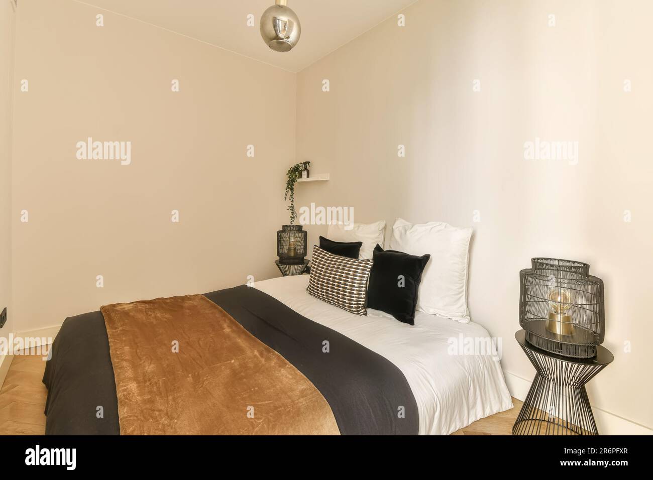 Ein Schlafzimmer mit weißen Wänden und Holzfußboden. Das Zimmer ist in neutralen Farbtönen mit schwarzen und goldenen Akzenten dekoriert Stockfoto