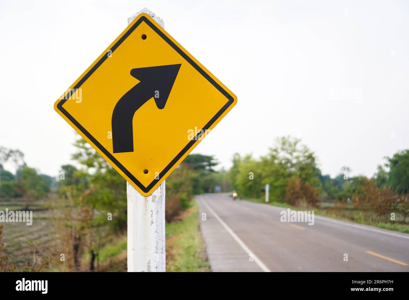 Ein Verkehrszeichen, das ein Warnschild in der rechten Kurve ist und eine Straße als Hintergrundkonzept hat oder für verschiedene Werbeanzeigen verwendet werden kann. Stockfoto