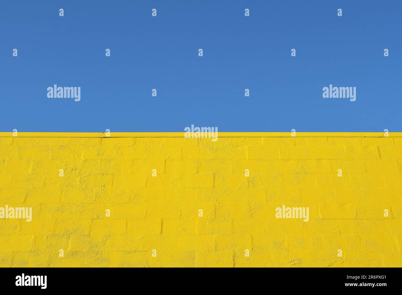 Ein blauer Himmel und eine starke gelbe Backsteinmauer im Design der ukrainischen Flagge als Symbol für die Stärke und Widerstandsfähigkeit des ukrainischen Volkes Stockfoto