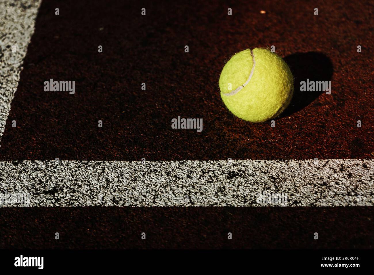 Ein lebendiger gelber Tennisball auf dem Platz mit weißen Linien an der Seite Stockfoto